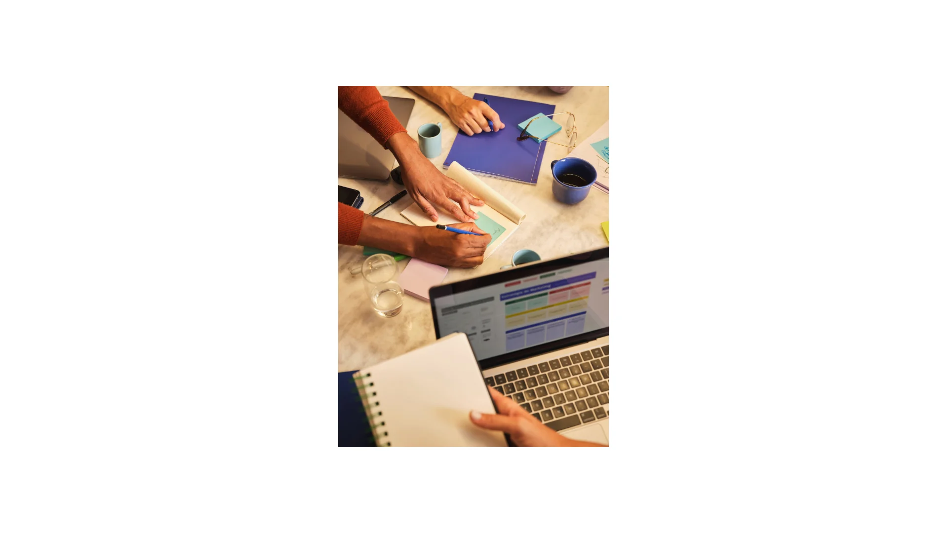 Hands taking project notes beside a laptop and planning materials